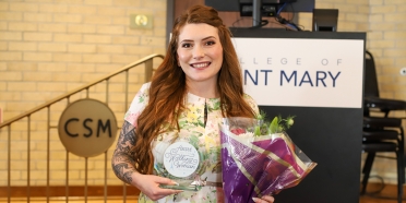 College of Saint Mary student Alexis Winter wears a floral dress and poses with a bouquet of flowers and her Heart of the Walking Woman award.