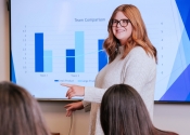 A woman gives a presentation in front of a screen with a chart. 